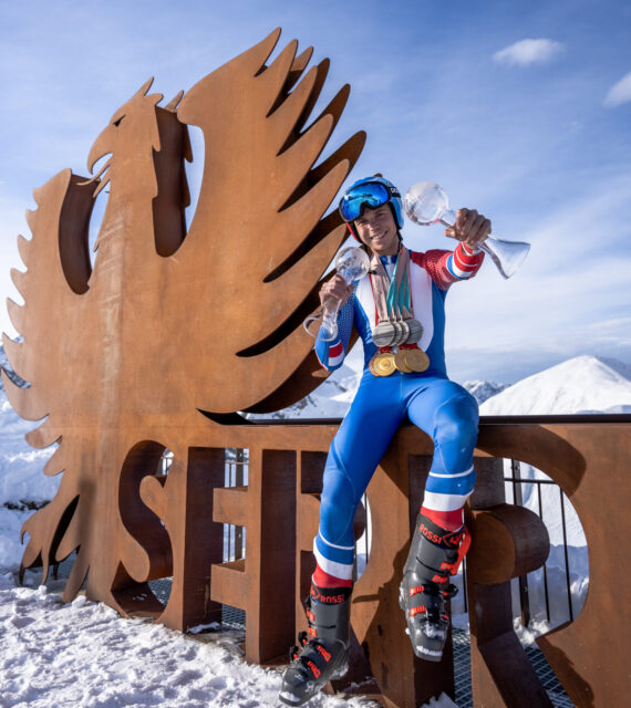 Arthur Bauchet pose, souriant, avec toutes ces récompenses sur le logo de Serre Chevalier